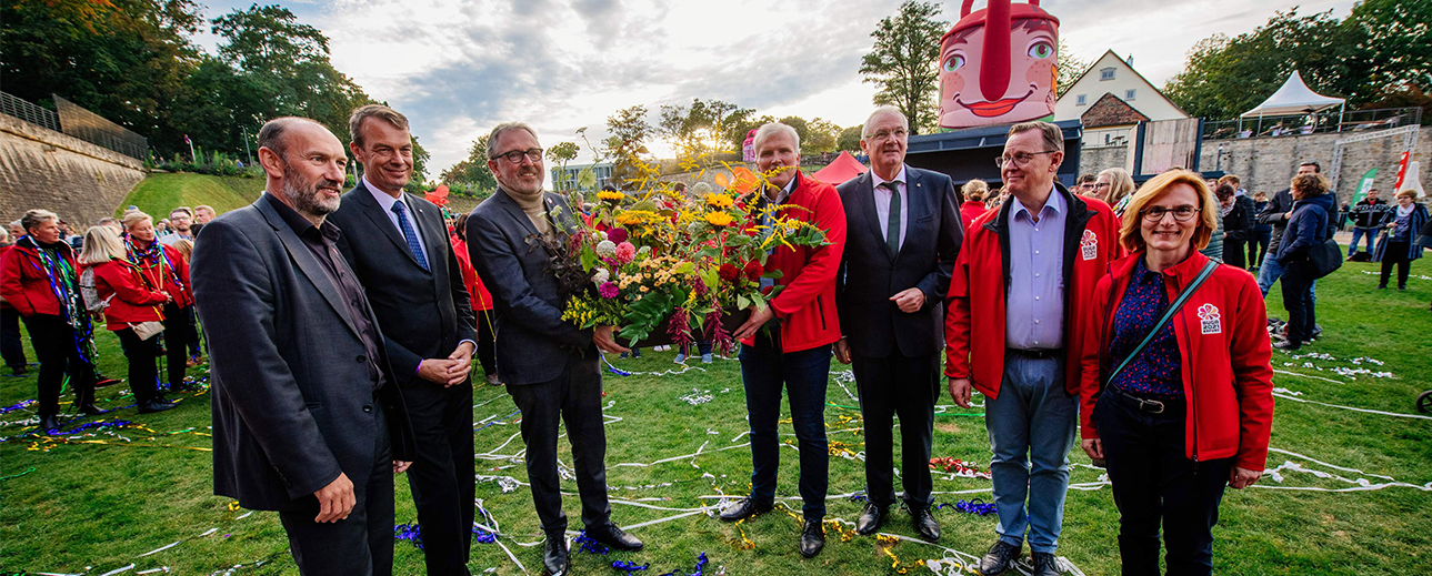 Sieben Menschen, darunter Oberbürgermeister Dr. Peter Kurz und BUGA 23 Geschäftsführer Michael Schnellbach stehen in einem Halbkreis und halten einen Blumenstrauß