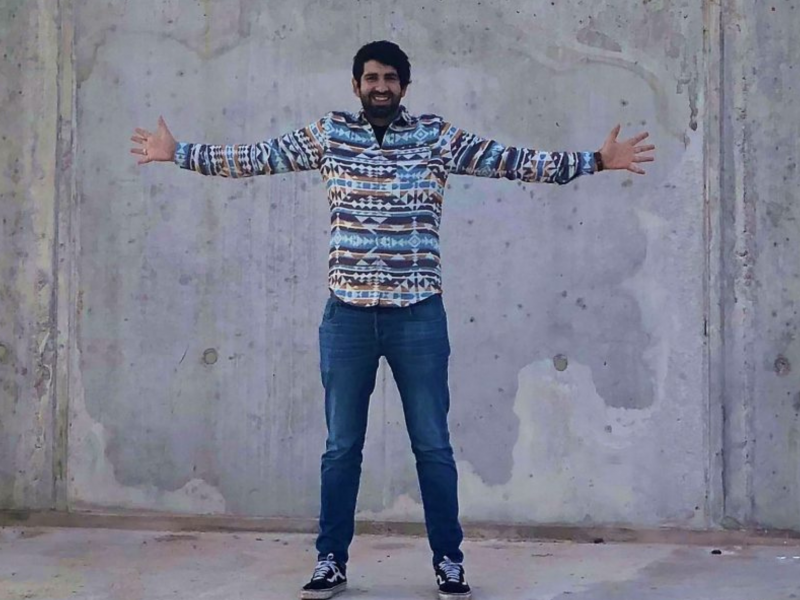 Farsad Tawakol steht mit stylischem sweater und ausgestreckten Armen vor einer Betonwand