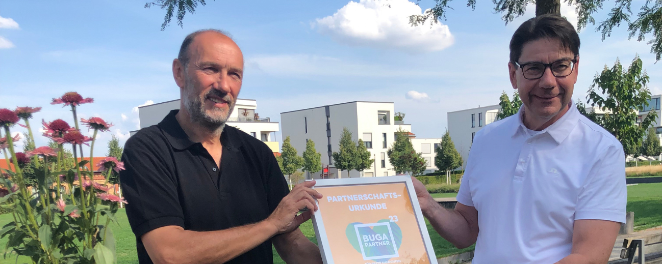 Michael Schnellbach, Geschäftsführer der BUGA 23 und Thomas Hirsch, Oberbürgermeister von Landau halten die orangene Partnerschaftsurkunde in der Hand