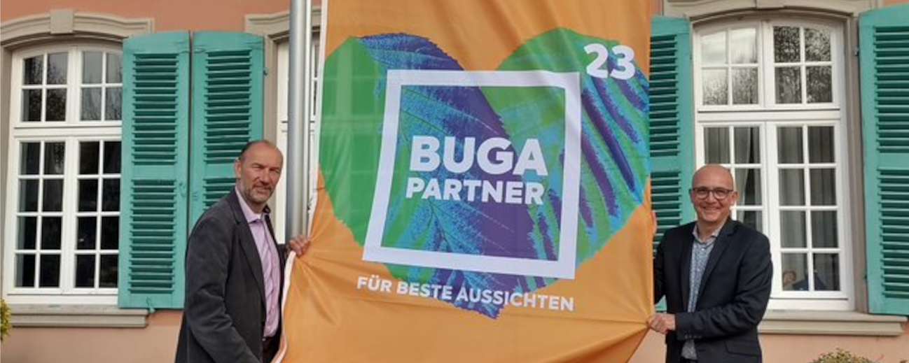 Buga-Geschäftsführer Michael Schnellbach und Schwetzingens Oberbürgermeister René Pöltl Halten die BUGA-Partnerflagge in der Hand