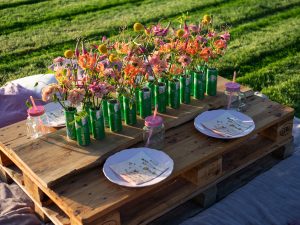 Europalette, die als Picknicktisch genutzt wird auf einer grünen Wiese. Red Bull Dosen in der Mitte werden als Blumenvasen genutzt