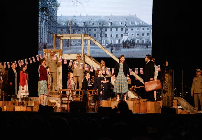 Eine Szene aus dem Joy Fleming Musical. Verschiedene Menschen, darunter einige amerikanische Soldaten stehen auf der Bühne