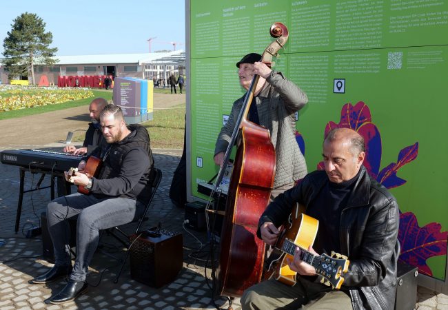 Vier Musikanten musizieren vor einem Informationskubus