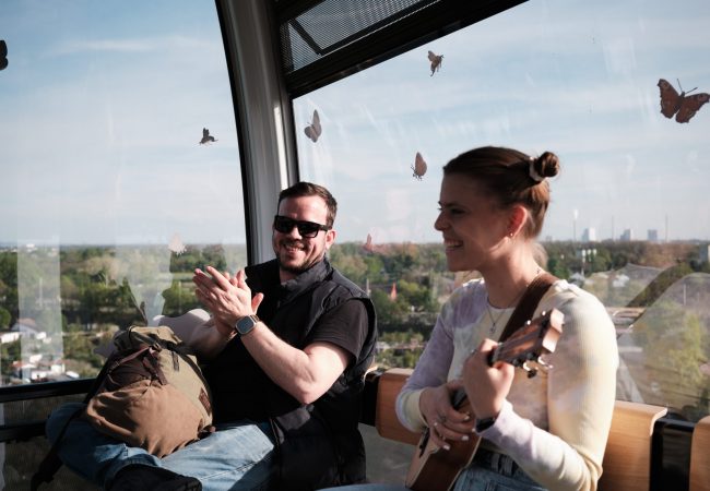 Eine Frau spielt Gitarre in einer Seilbahnkabine. ein Passagier applaudiert