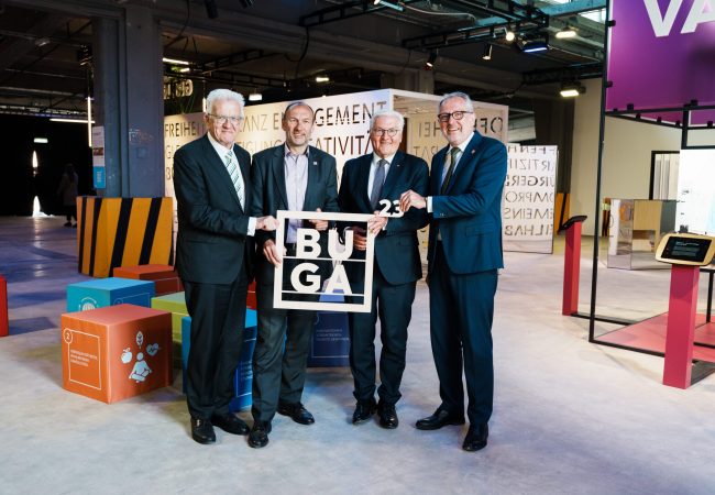Winfried Kretschmann, Michael Schnellbach, Frank Walter Steinmeier und Peter Kurz halten ein BUGA 23 Logo aus Holz