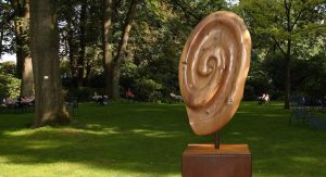 Eine große Holzskulptur in Form eines Ohrs steht auf einer Wiese